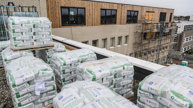 Stapels zakken met lichtgewicht cementdekvloer materiaal op een bouwplaats, met een gebouw in aanbouw op de achtergrond.